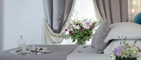 A neatly made bed with a bouquet of flowers, a tray with pastries, and a bedside table with a lamp.