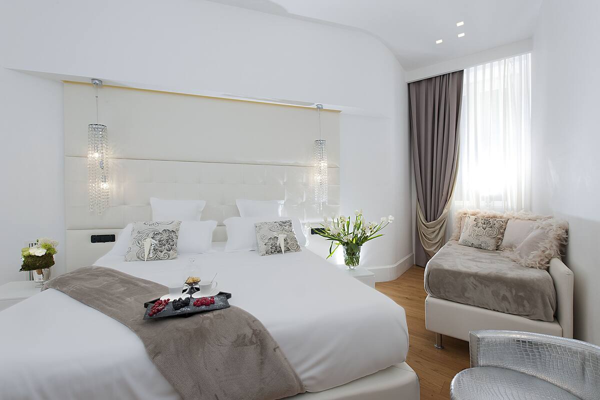 A modern bedroom with a large bed, a smaller sofa, and a dining table with fruit.