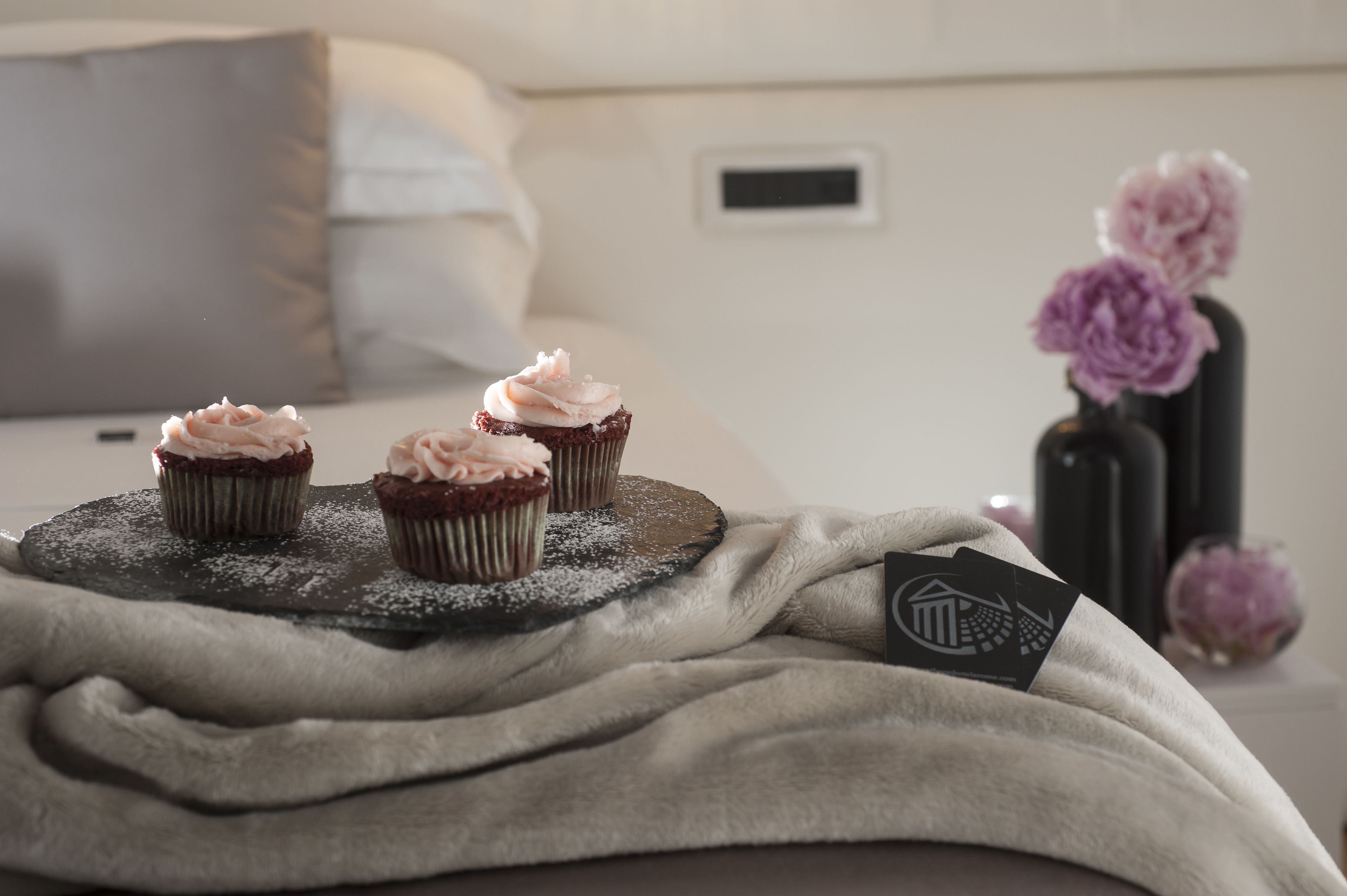 A bed with a blanket and three cupcakes on a wooden board.