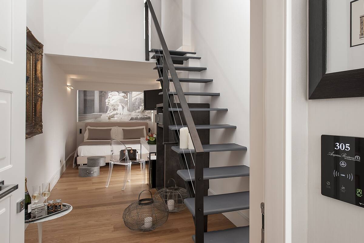 A modern interior with a staircase, a bed, a dining area, and a wall-mounted control panel.