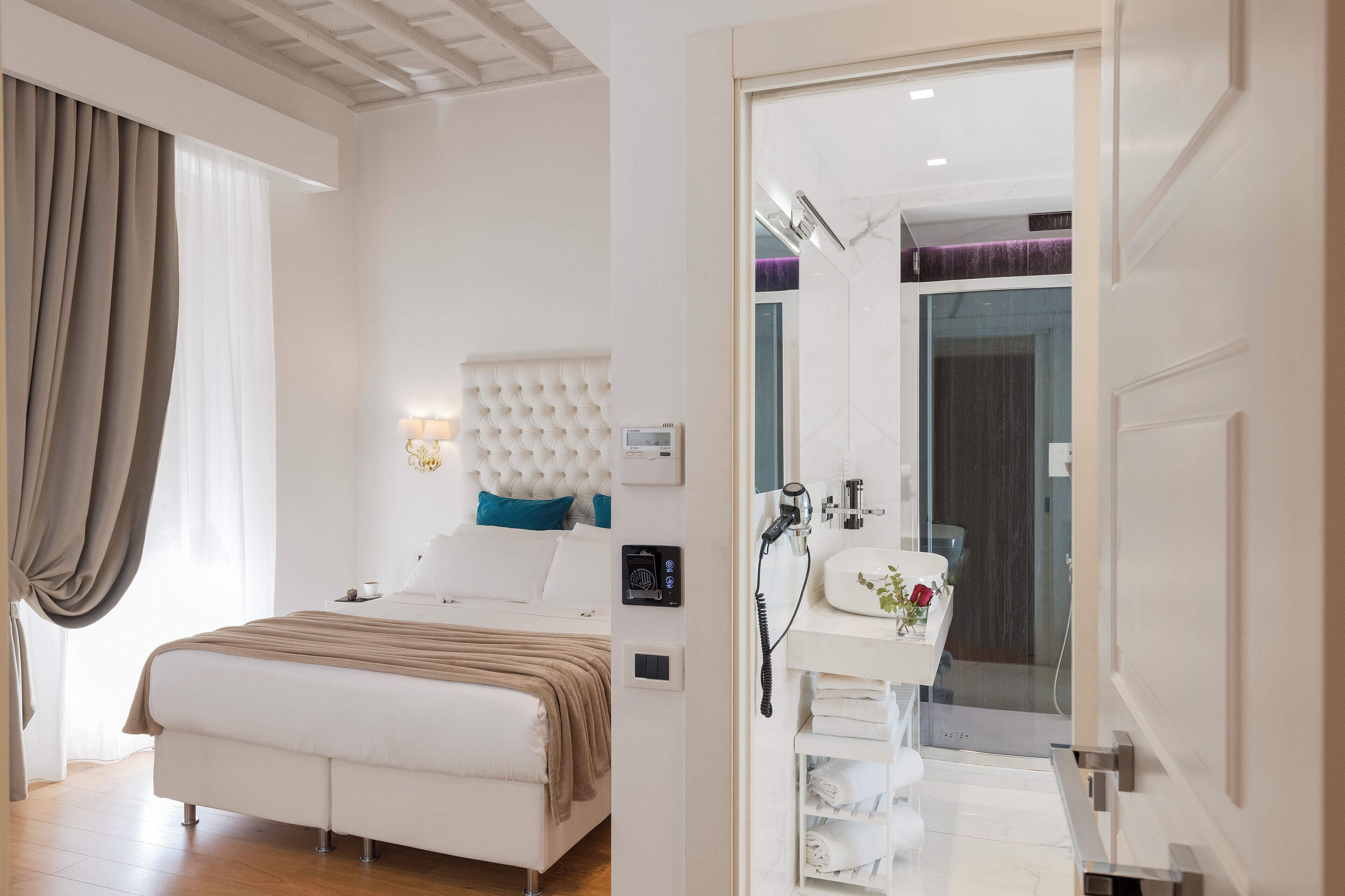 A modern bedroom with a large bed, a bedside table, a built-in headboard, and a bathroom with a sink and mirror.