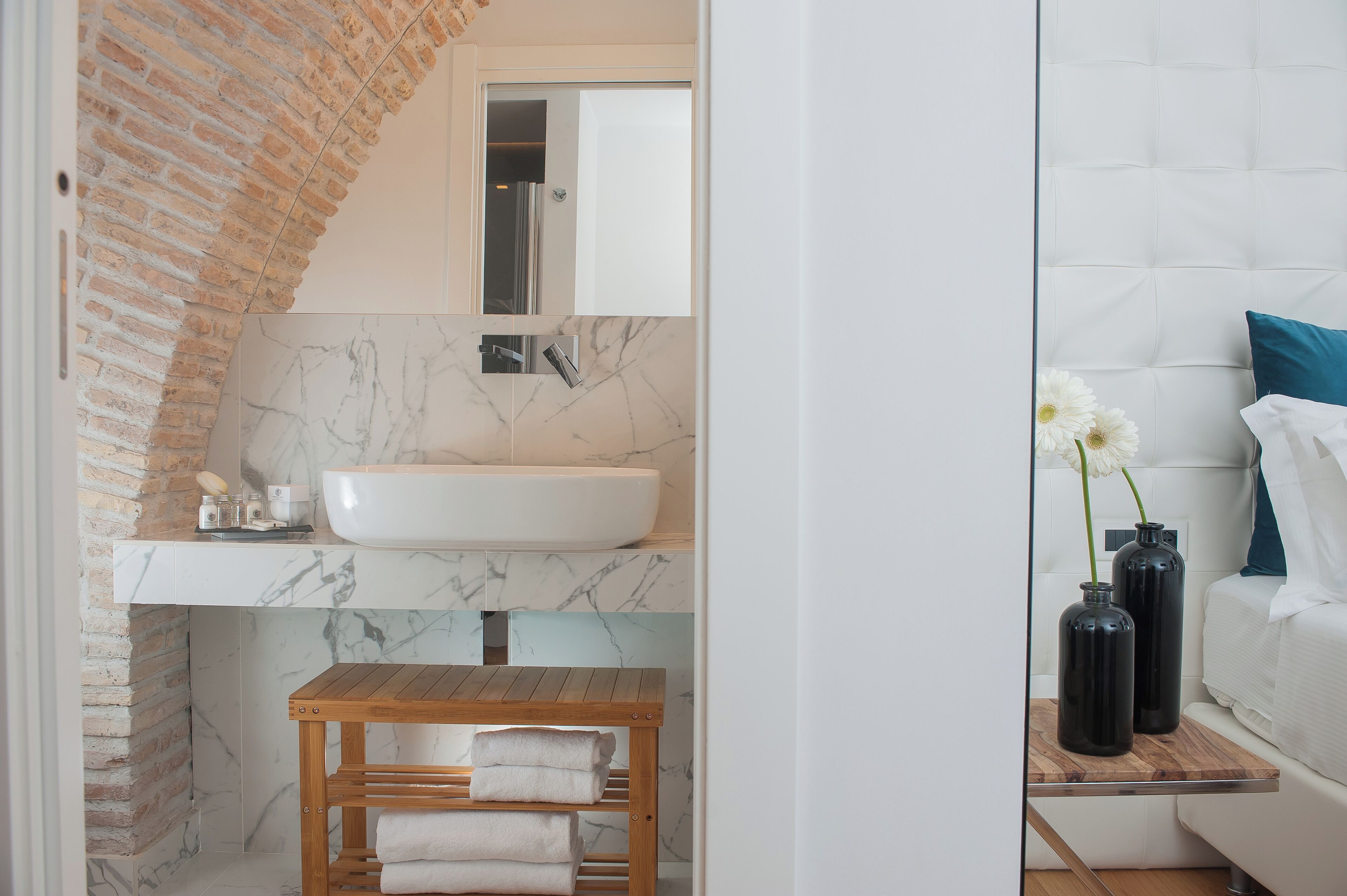 Un baño con lavamanos blanco, salpicadero de mármol y un banco de madera con toallas.