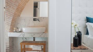 Un baño con lavamanos blanco, salpicadero de mármol y un banco de madera con toallas.