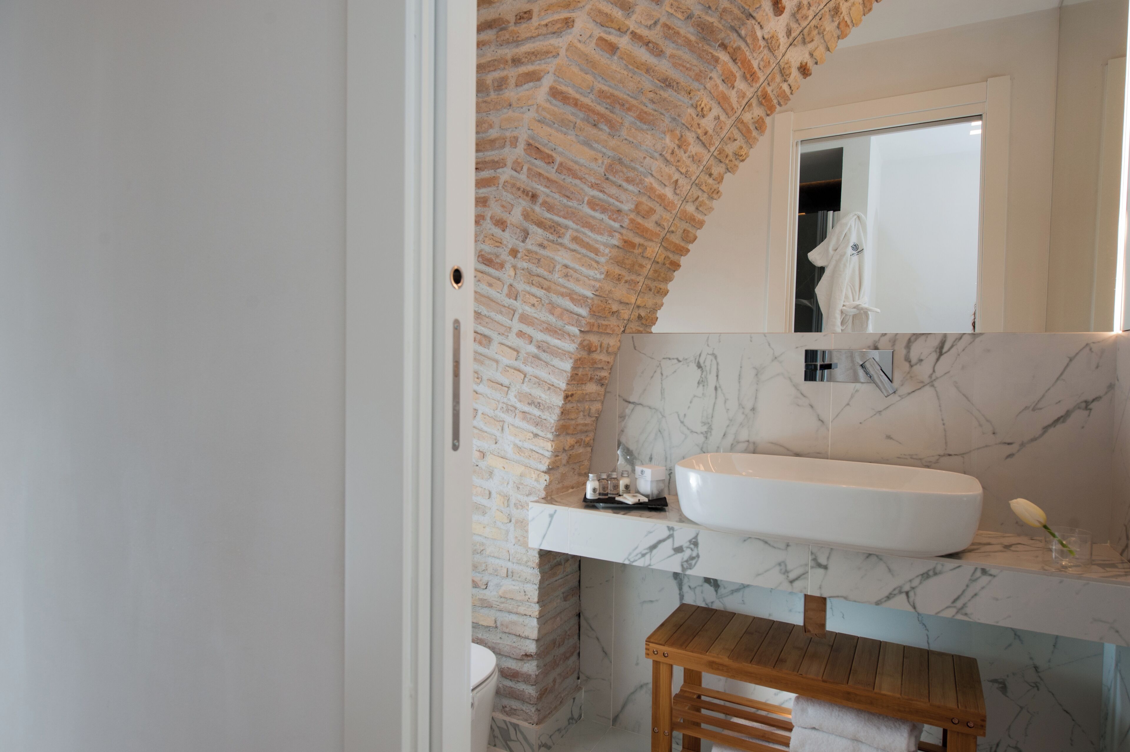 A bathroom with a white sink, marble countertop, and a wooden bench.