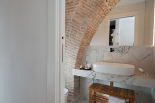 A bathroom with a white sink, marble countertop, and a wooden bench.