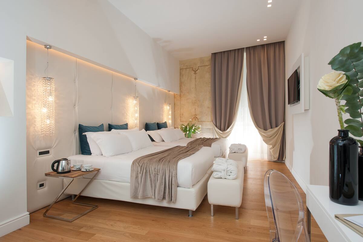 A modern bedroom with a large bed, bedside tables, a small seating area, and a large window with curtains.