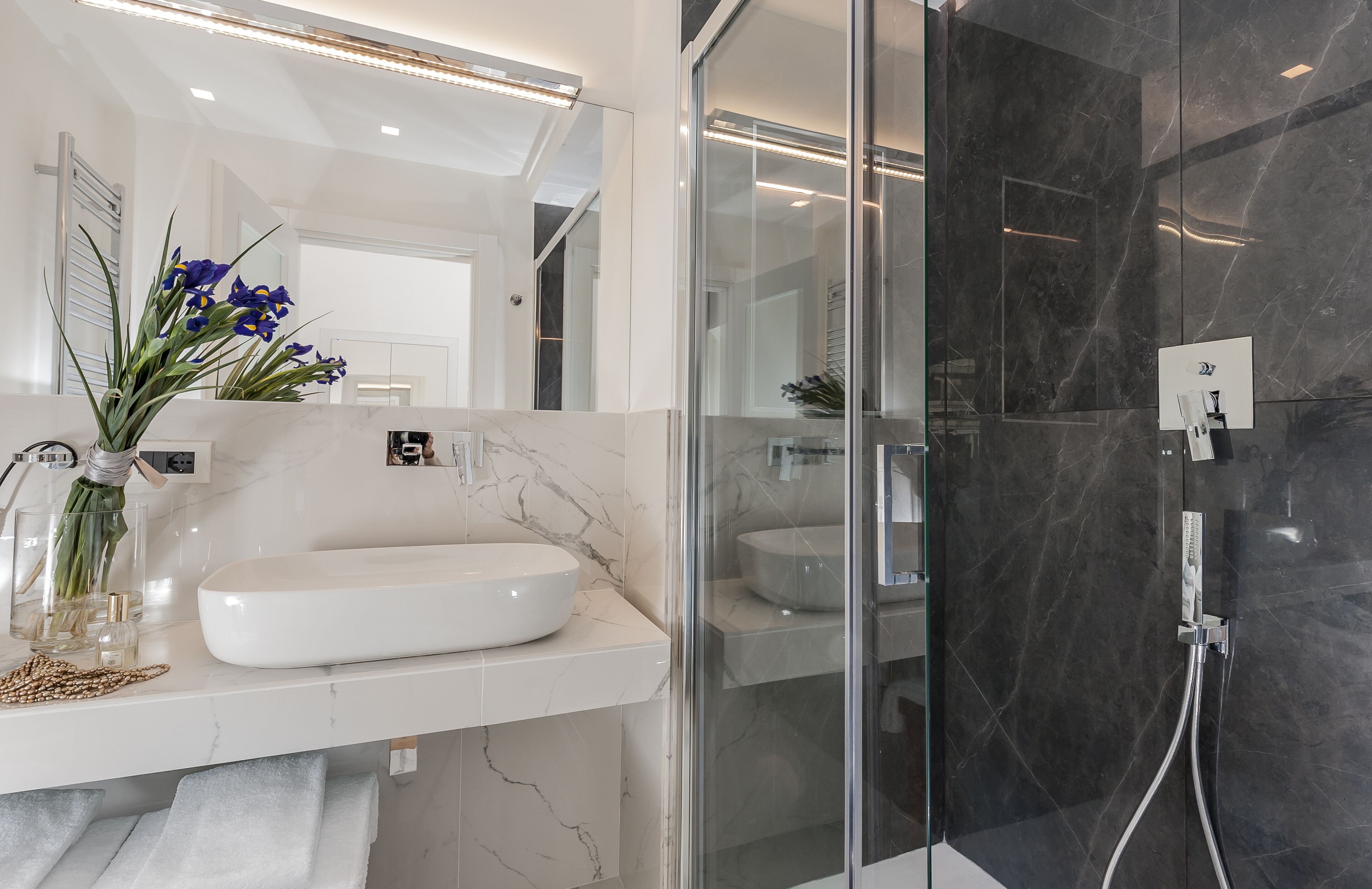 Une salle de bain moderne avec un lavabo en marbre blanc, une douche en verre et un vase rempli de fleurs posé sur le comptoir.