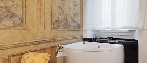 A bathroom with a large bathtub, a wooden chair, and a decorative wall.
