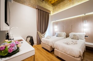 A hotel room with two beds, a desk with a vase of flowers, a mirror, and a ceiling with a decorative design.