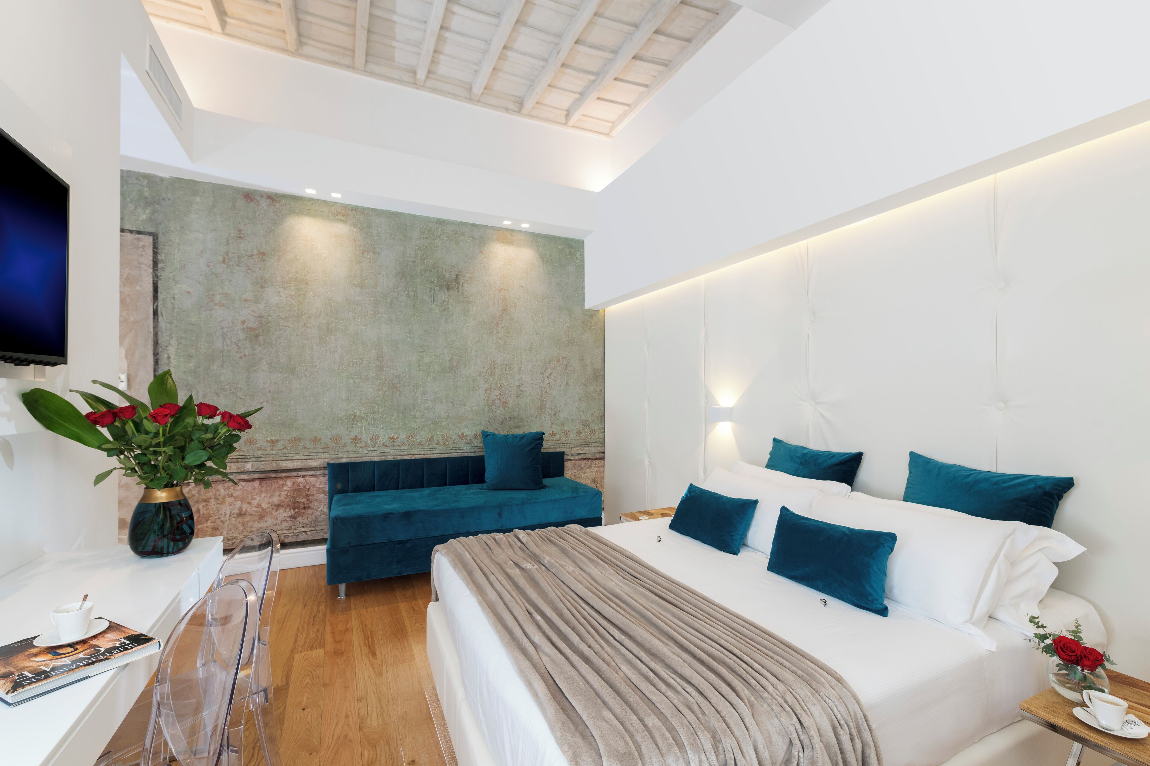 A modern bedroom with a large bed, a blue sofa, and a TV on the wall.