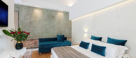 A modern bedroom with a large bed, a blue sofa, and a TV on the wall.