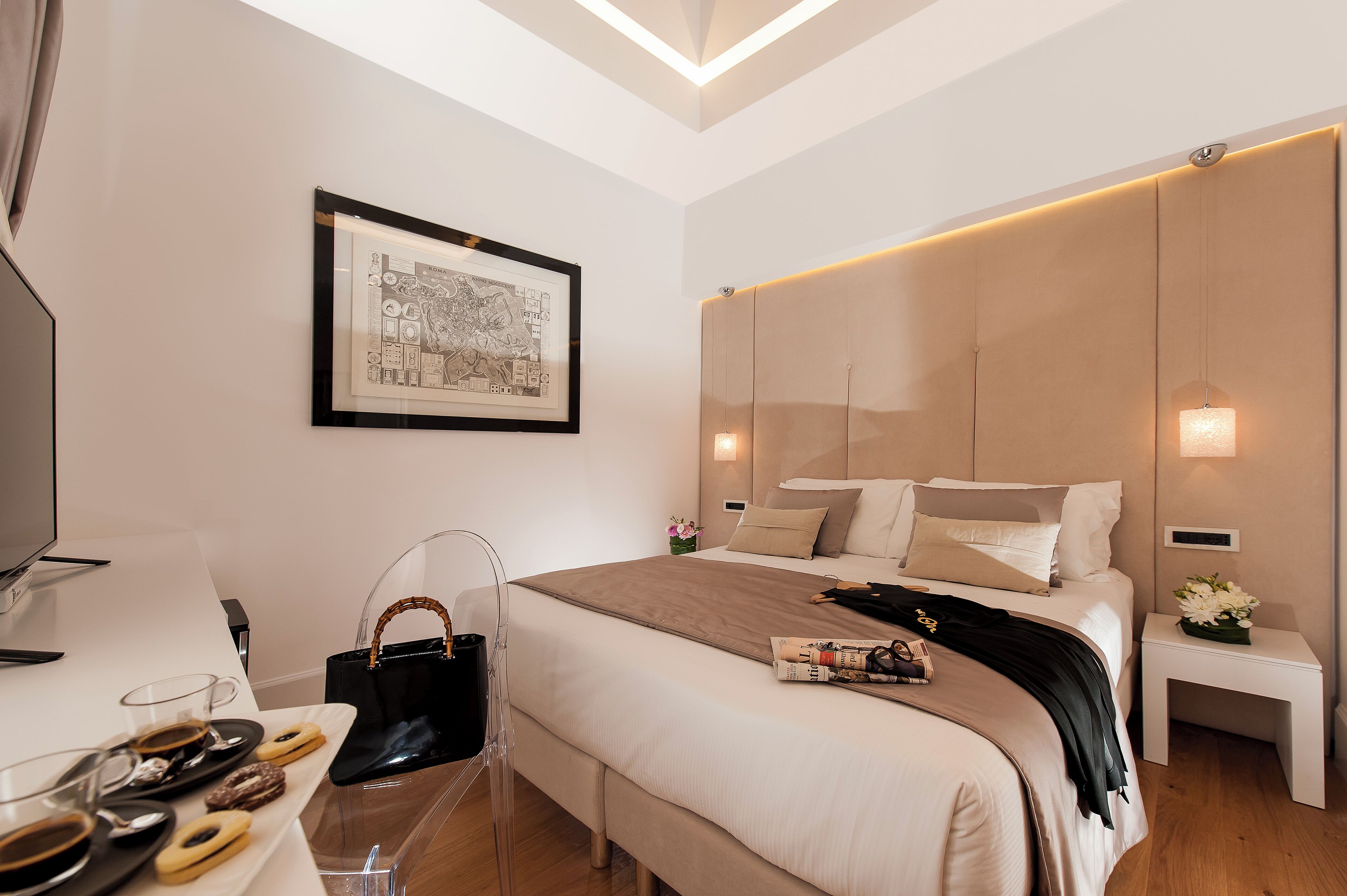 A modern hotel room with a large bed, a flat-screen TV, a clear glass chair, and a tray with pastries.