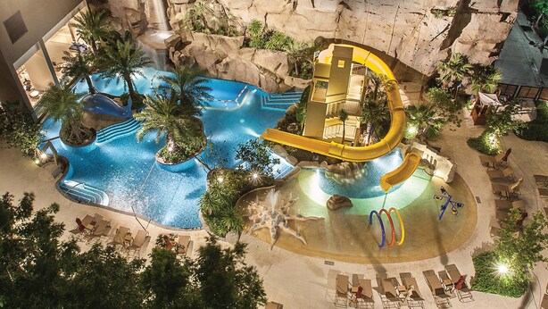 An aerial view of a hotel pool area with a water slide, multiple lounge chairs, and surrounding greenery. - Mercure Pattaya Ocean Resort (Pattaya)