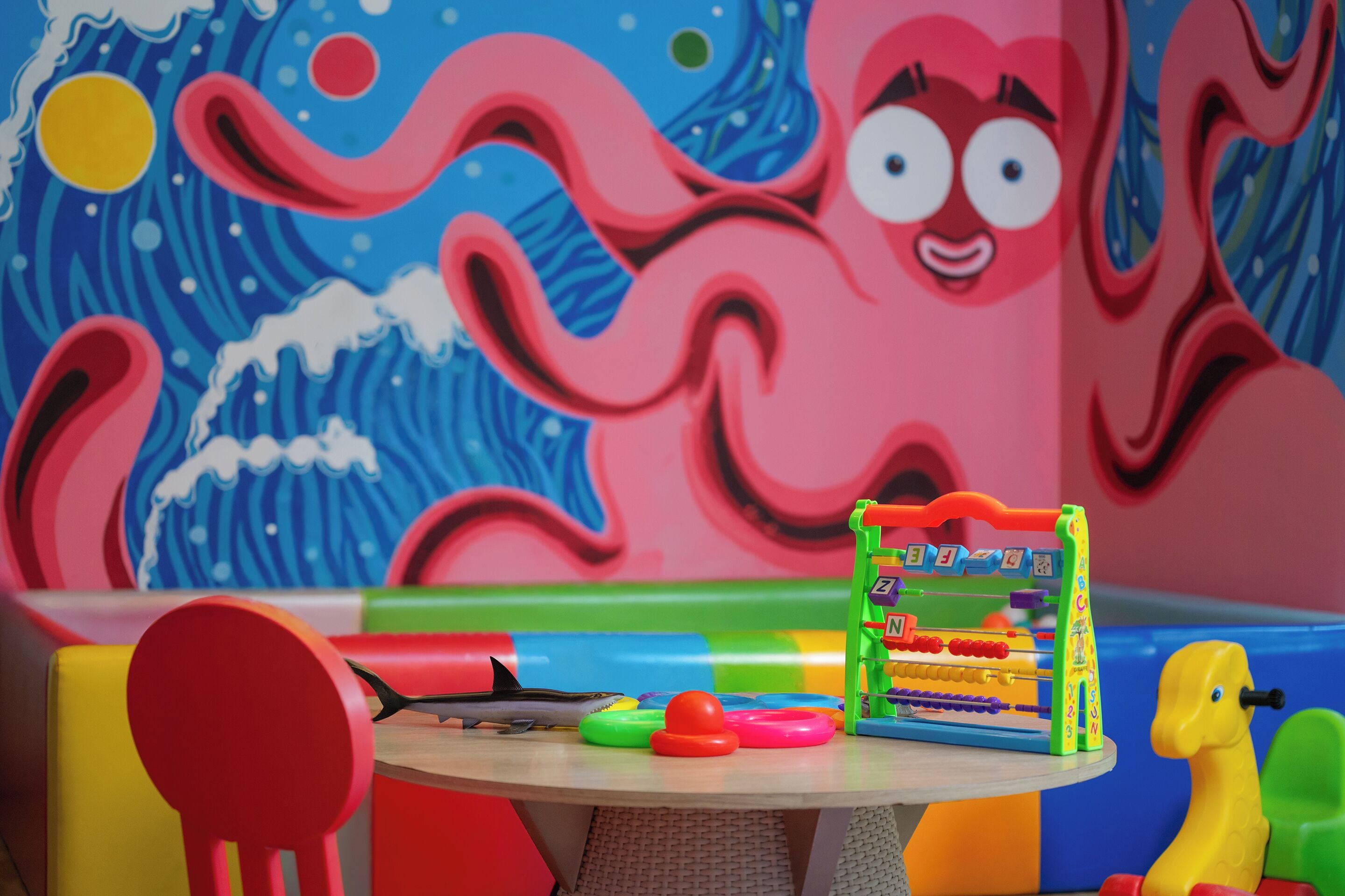 Una habitación colorida con un gran mural de pulpo, una mesita con juguetes y una jirafa de juguete amarilla.