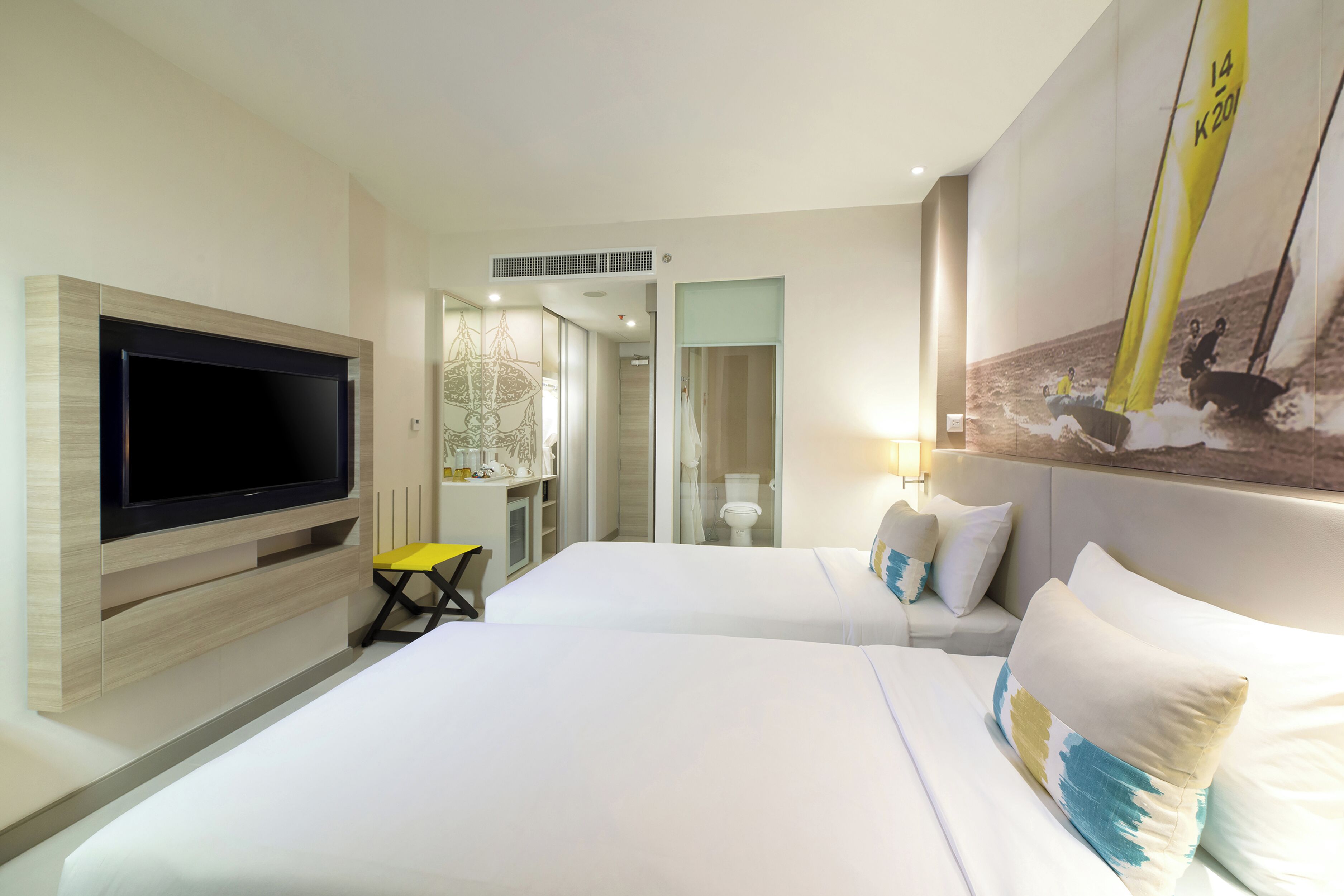 A hotel room with two beds, a flat-screen TV mounted on the wall, a small desk, and a mirror.
