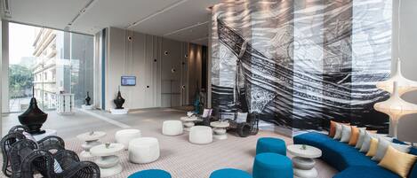 A modern lounge area with a large sofa, multiple seating options, and a large window offering a view of the city.