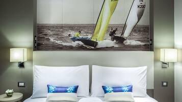A hotel room with a bed, two pillows, a nightstand, a lamp, and a wall-mounted picture of a sailboat.