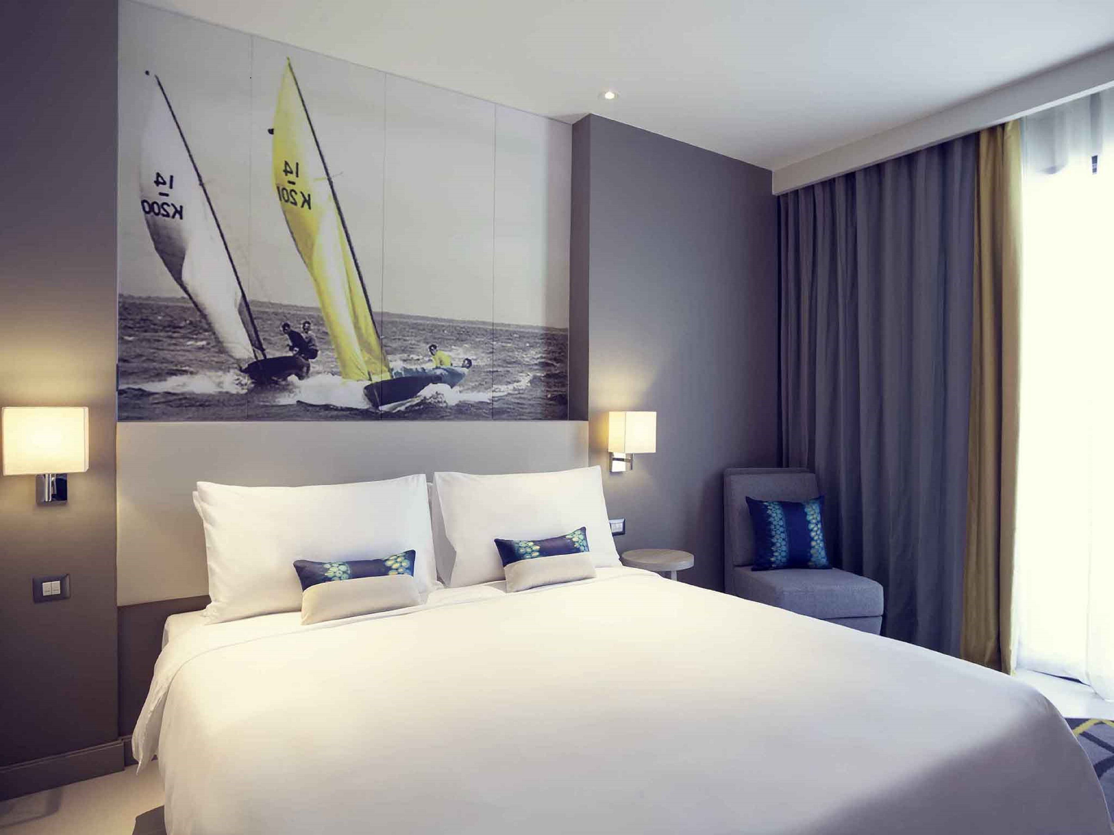A hotel room with a large bed, two bedside lamps, a chair, and a sailboat painting on the wall.