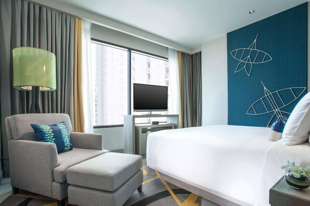 A hotel room with a bed, a TV, a desk, a chair, and a large window with curtains.