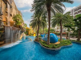 Un área de piscina con cascada, palmeras y una estatua de ballena azul.