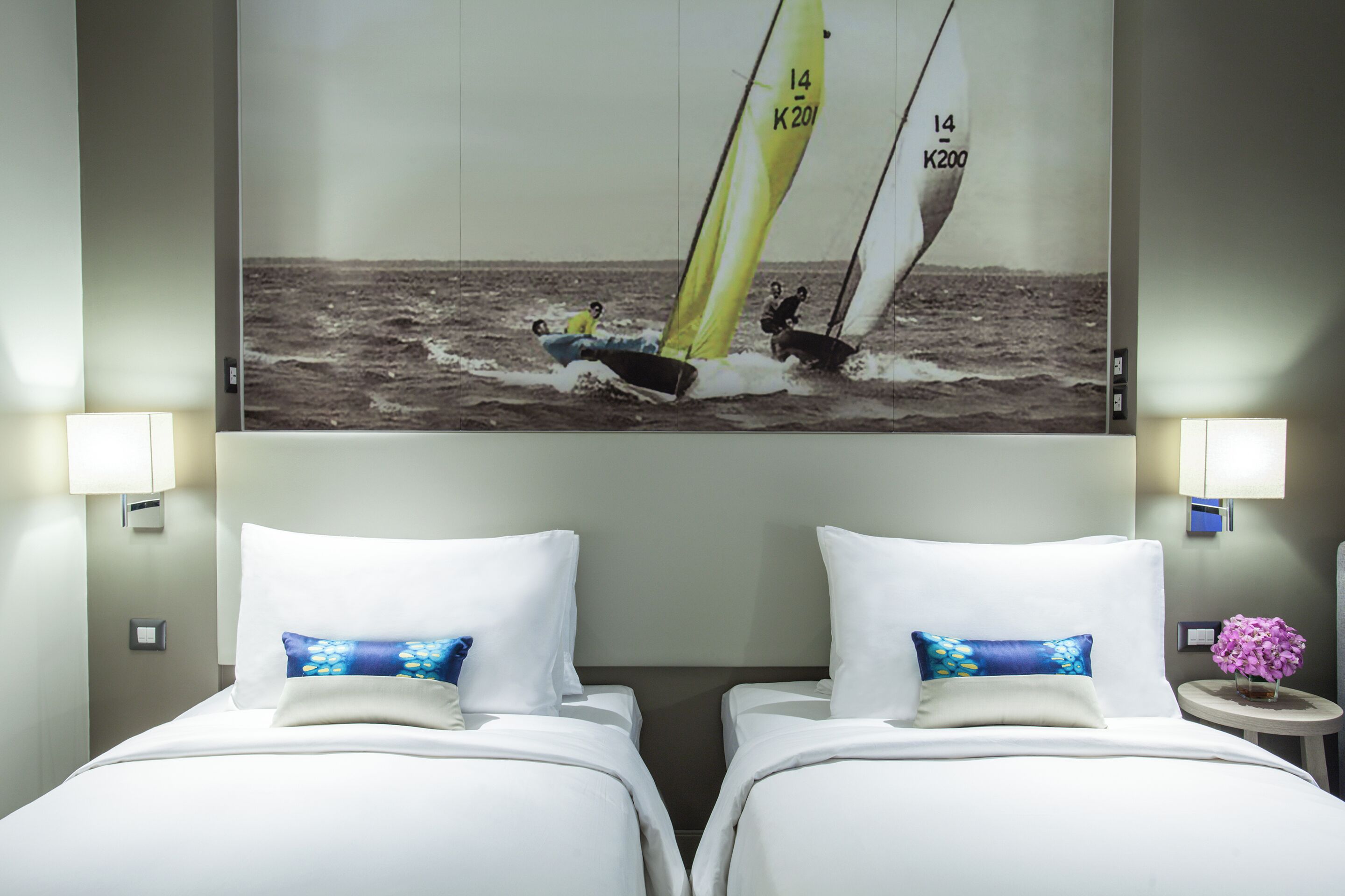 A hotel room with two beds, a large wall-mounted picture of a sailing boat, and bedside lamps.