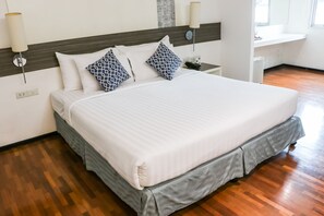 A neatly made bed with white and blue patterned pillows, a grey skirted bed base, and a wooden floor.