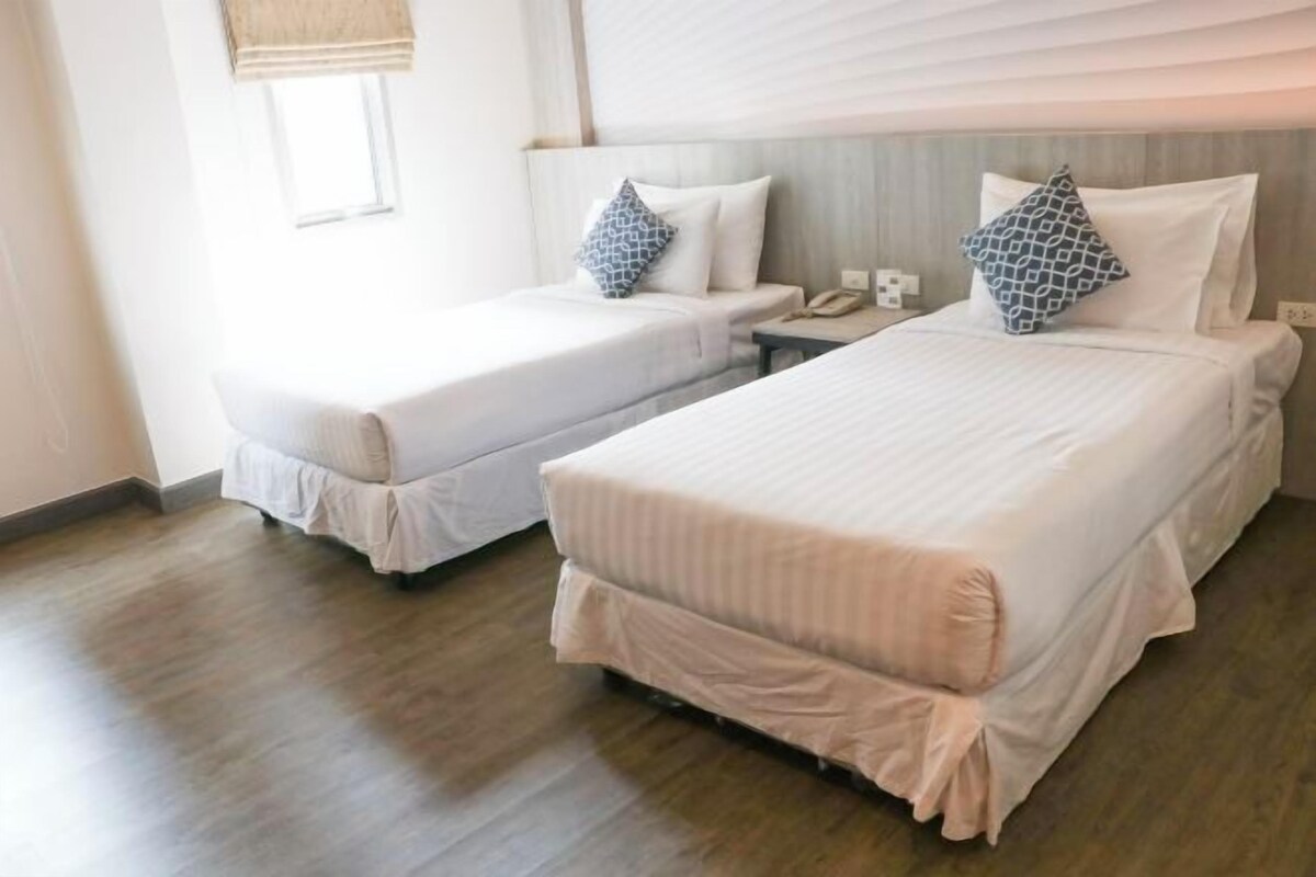 A hotel room with two beds, each with a pillow and a bedside table with a phone.