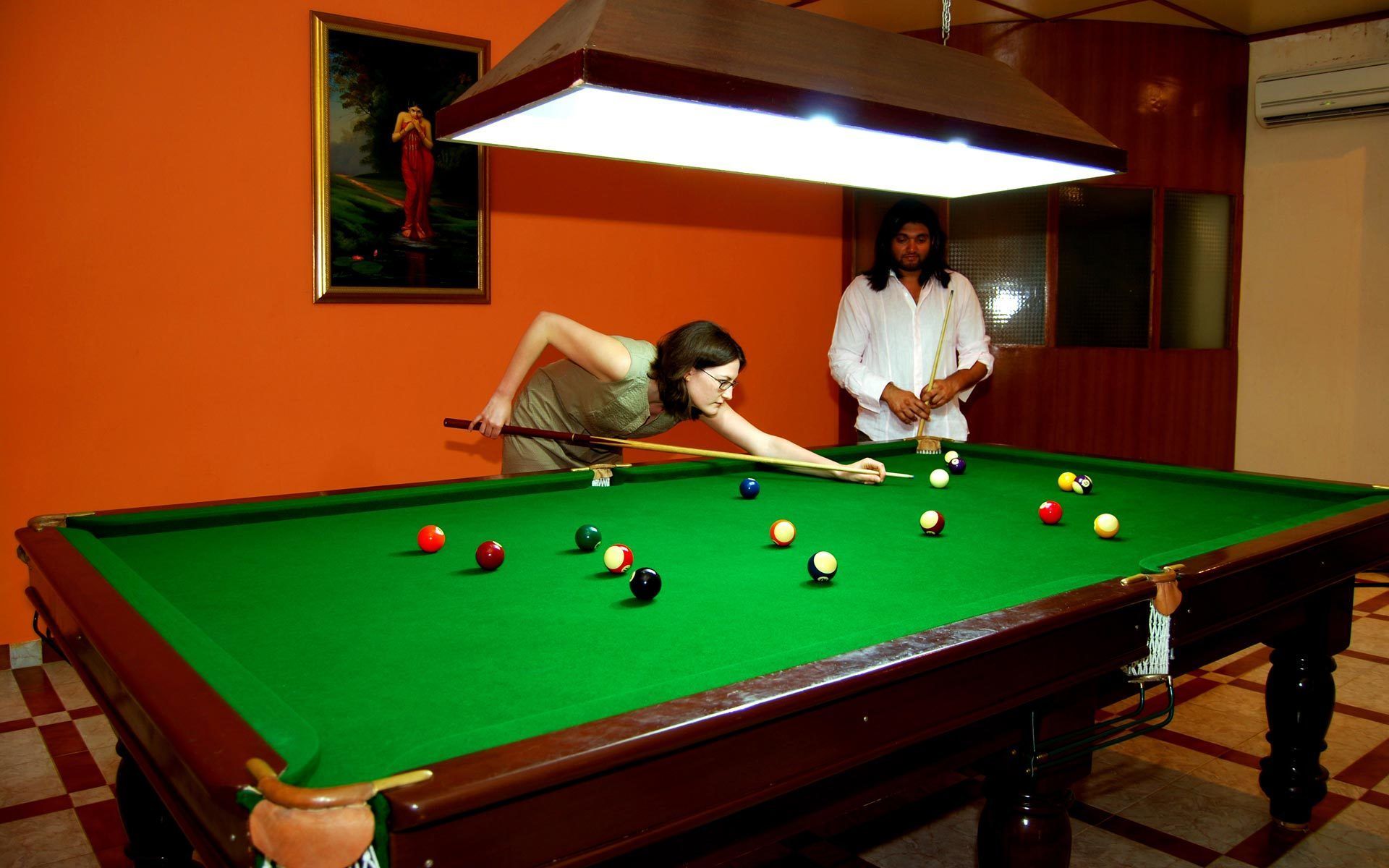 A pool table with balls, a person playing, and another observing.