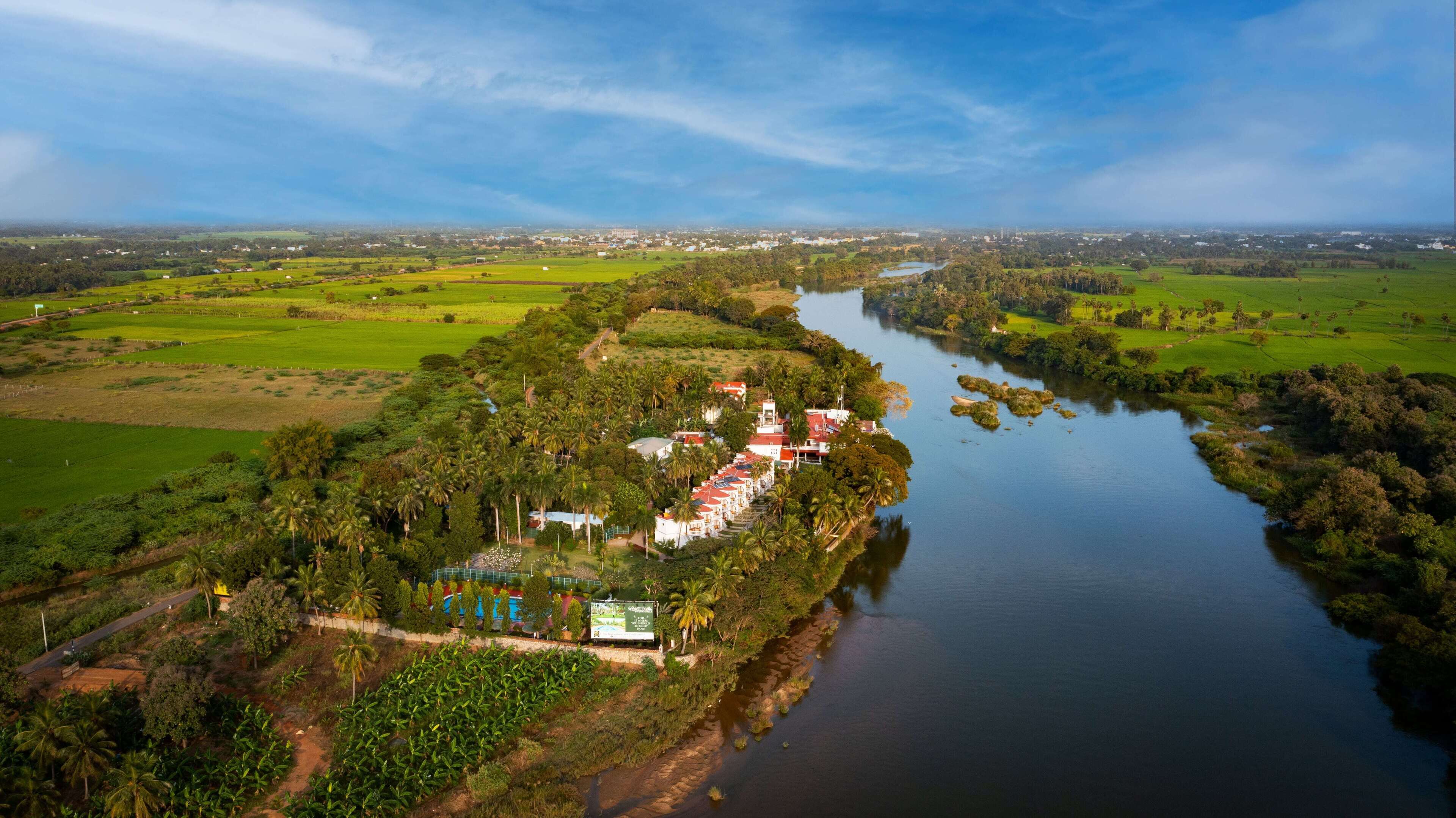 An aerial view of a riverside property with a row of white buildings, a swimming pool, and lush greenery.