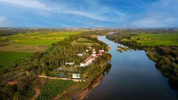 An aerial view of a riverside property with a row of white buildings, a swimming pool, and lush greenery.