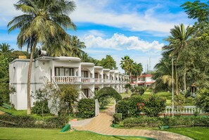 Un resort con varias edificaciones blancas, un camino central y abundante vegetación, incluyendo palmeras.