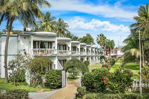 A row of white, two-story buildings with balconies, surrounded by lush greenery and palm trees. - Great Trails River View Resort Thanjavur by GRT Hotels (Thanjavur)