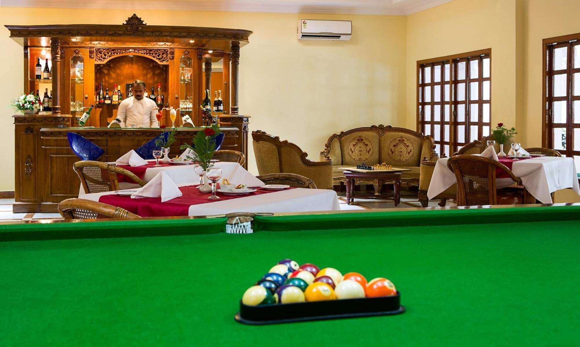 A billiards table with balls, a bar area with a bartender, and a seating area with a sofa and chairs.