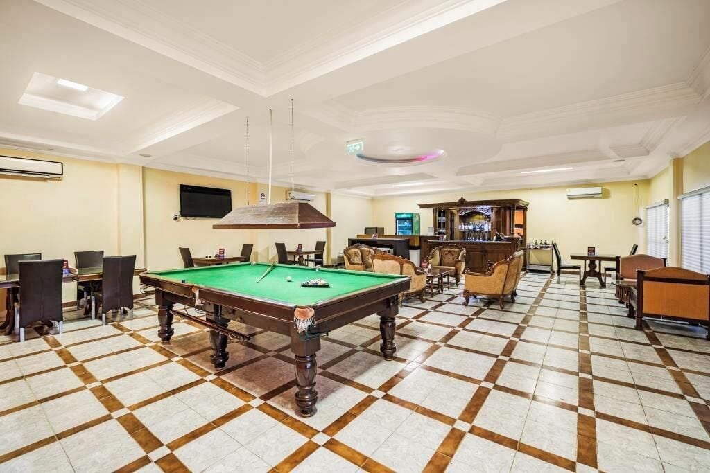 A billiards room with a pool table, chairs, and a bar area.