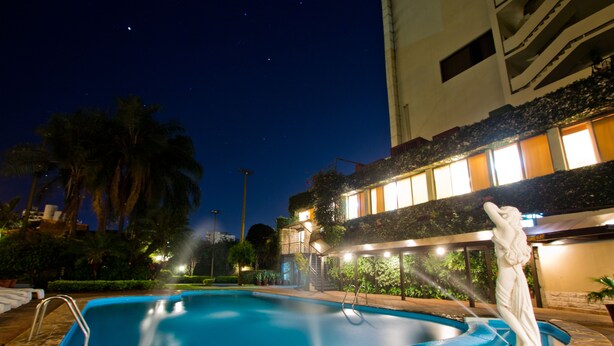 Una piscina con una estatua, rodeada de palmeras y un edificio con ventanas iluminadas.