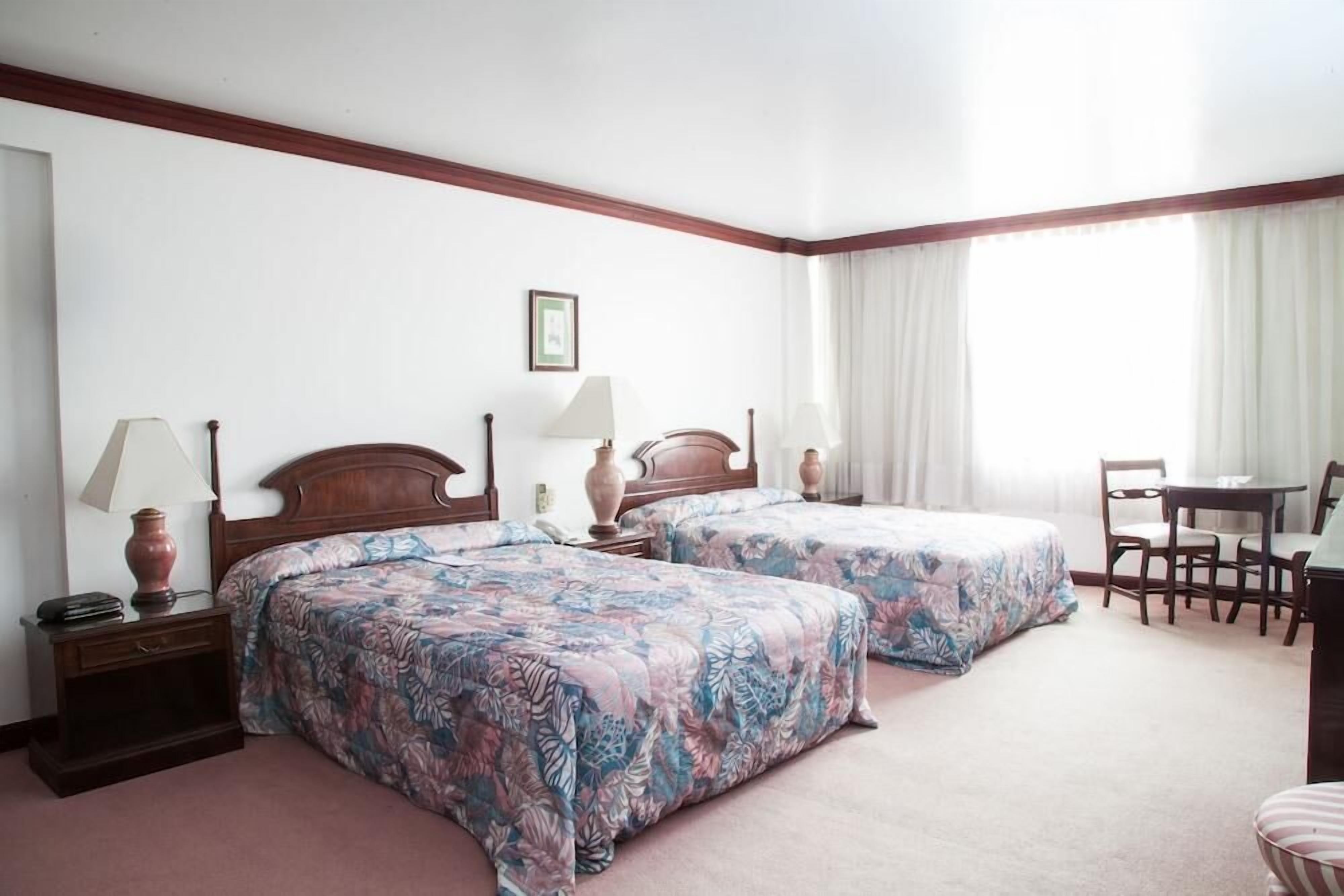 A hotel room with two beds, a desk, and a chair.