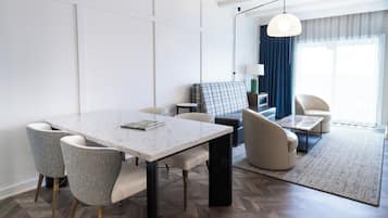 Una camera d'albergo moderna con zona pranzo, divano, tavolino e vista sull'esterno.