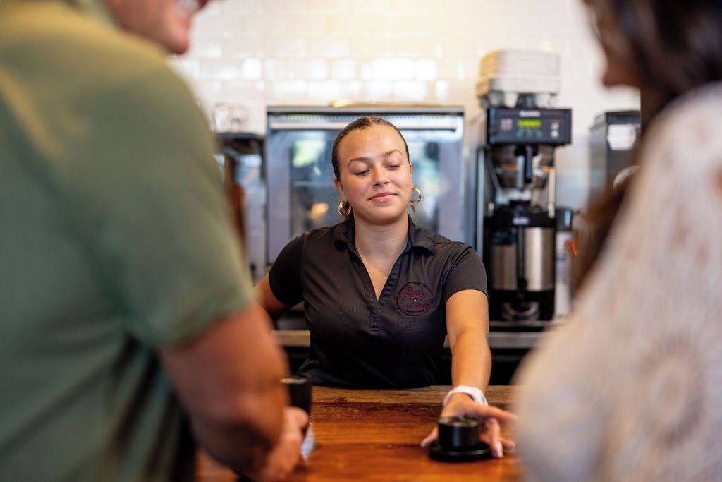 Una persona seduta al bancone, con una macchina per il caffè sullo sfondo.