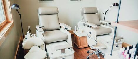 Een moderne nagelsalon met twee ruime stoelen, een klein tafeltje en diverse producten voor nagelverzorging.