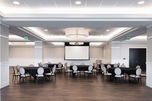 A conference room with multiple tables and chairs, a large screen, and a chandelier.