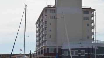 Un port de plaisance où sont amarrés plusieurs bateaux, un grand immeuble doté de balcons et un ciel dégagé.