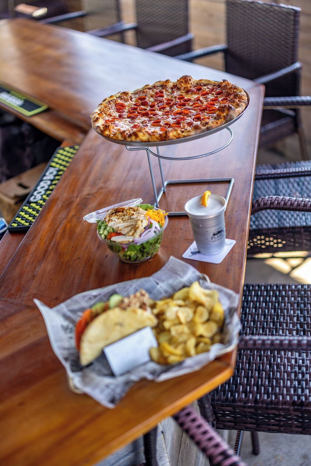 A wooden table with a pizza, salad, and chips.