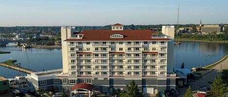 A multi-story hotel with a central courtyard, parking lot, and a view of a body of water.