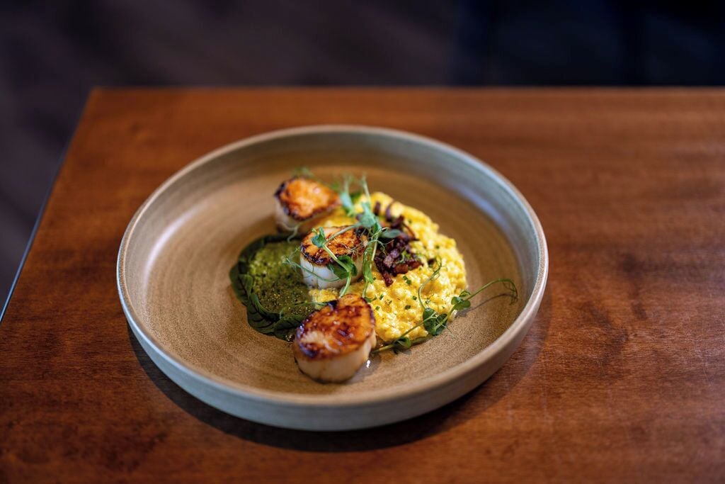 A plate of food with seared scallops, greens, and a creamy sauce.