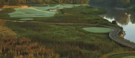 Un campo de golf con varios greens, un cuerpo de agua y un camino sinuoso.
