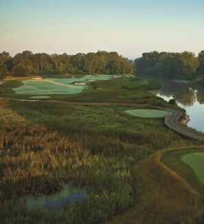 A golf course with multiple greens, a water body, and a winding road.