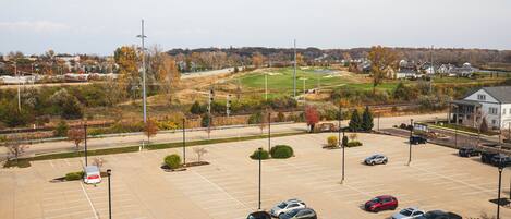 A parking lot with multiple cars and a few trucks, surrounded by trees and buildings in the background.