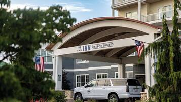 La entrada de un hotel con una bandera estadounidense, una camioneta SUV blanca estacionada al frente y un edificio con balcones.