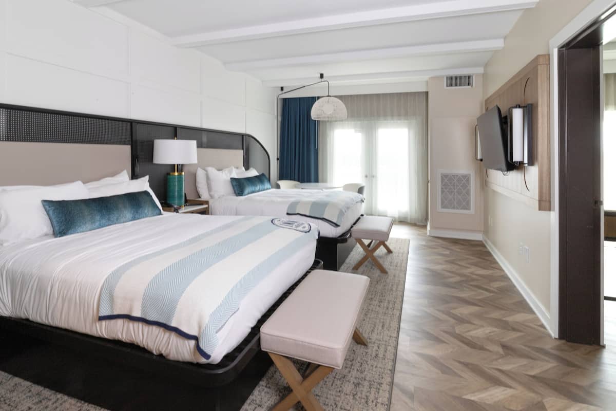 Ein Hotelzimmer mit zwei Betten, einem Schreibtisch, einem Sessel, einem Fernseher und einem großen Fenster mit Vorhängen.