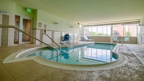 An indoor swimming pool with a tiled floor, a lifeguard chair, and a view of the outdoors through large windows.